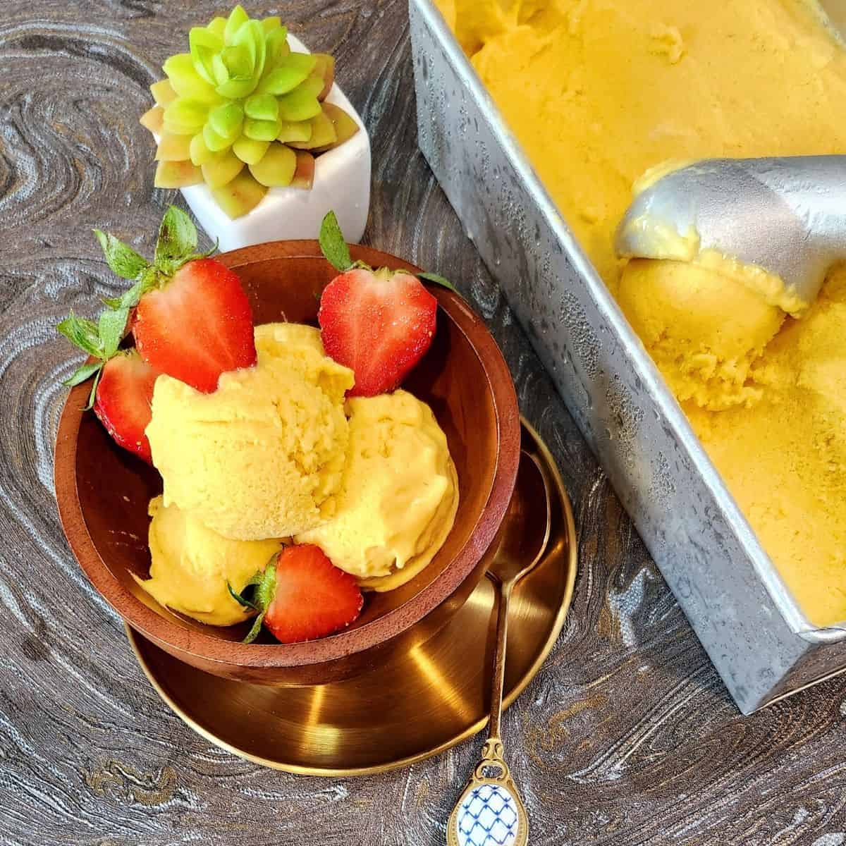 A bowl of mango ice cream with strawberries and a spoon.