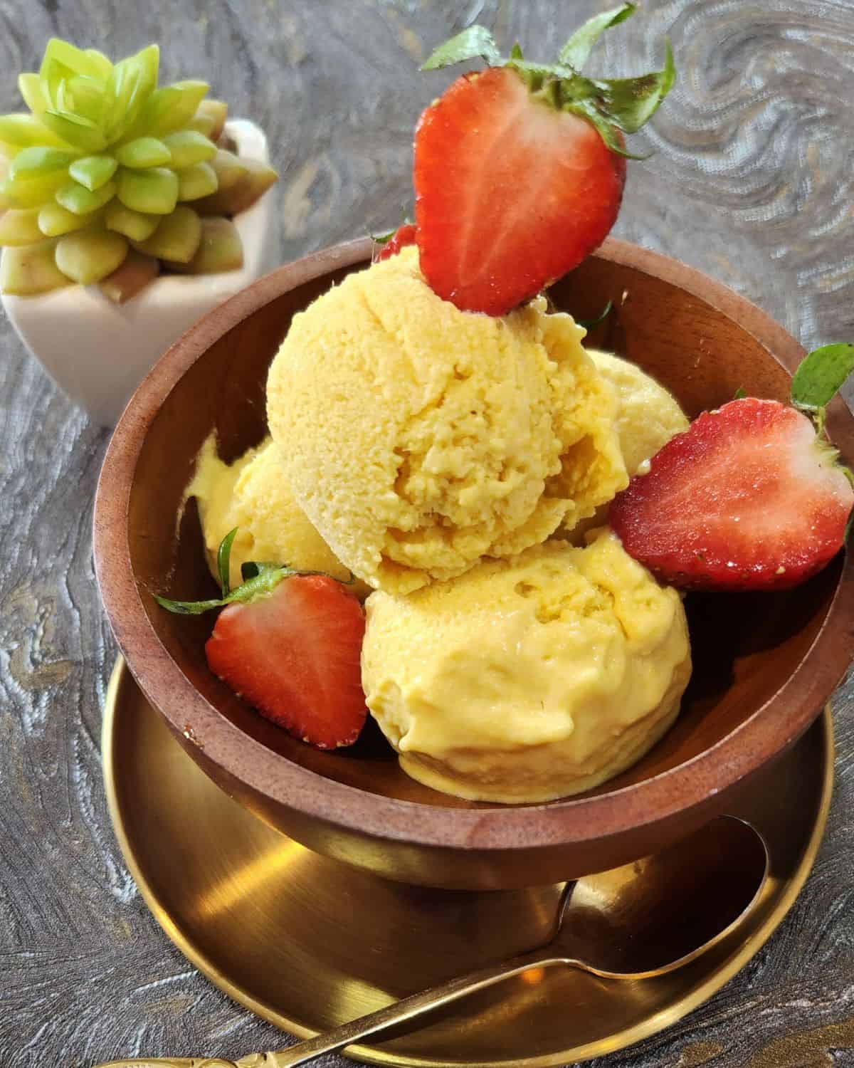 A bowl of mango ice cream with strawberries and a spoon.