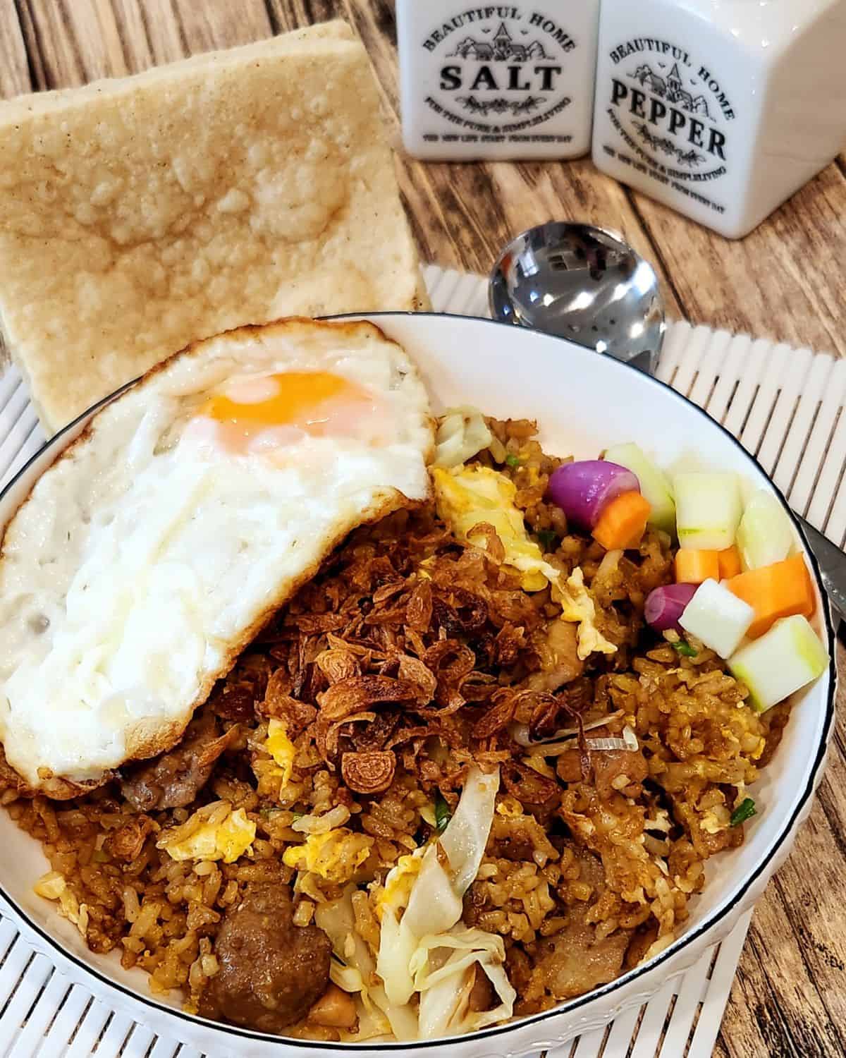 A plate of nasi goreng kampung with sunny side up egg and some pickles.