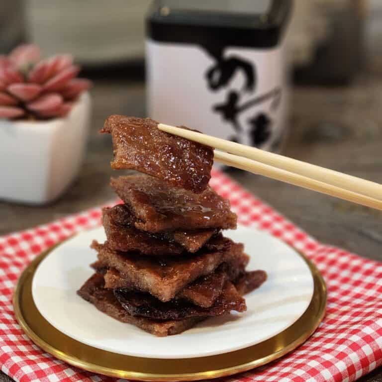 A plate of pork jerky slices with a pair of chopsticks holding one slice.