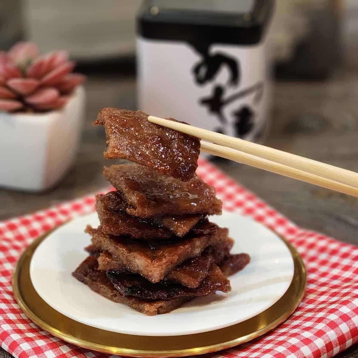 A plate of pork jerky slices with a pair of chopsticks holding one slice.