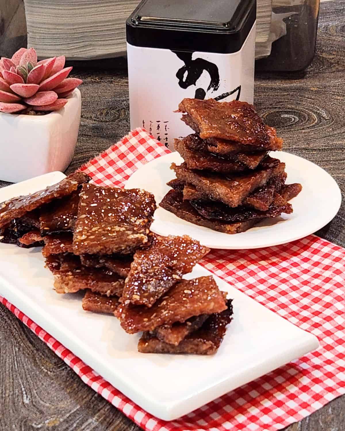 A rectangular plate of pork jerky slices and a round plate of pork jerky slices.