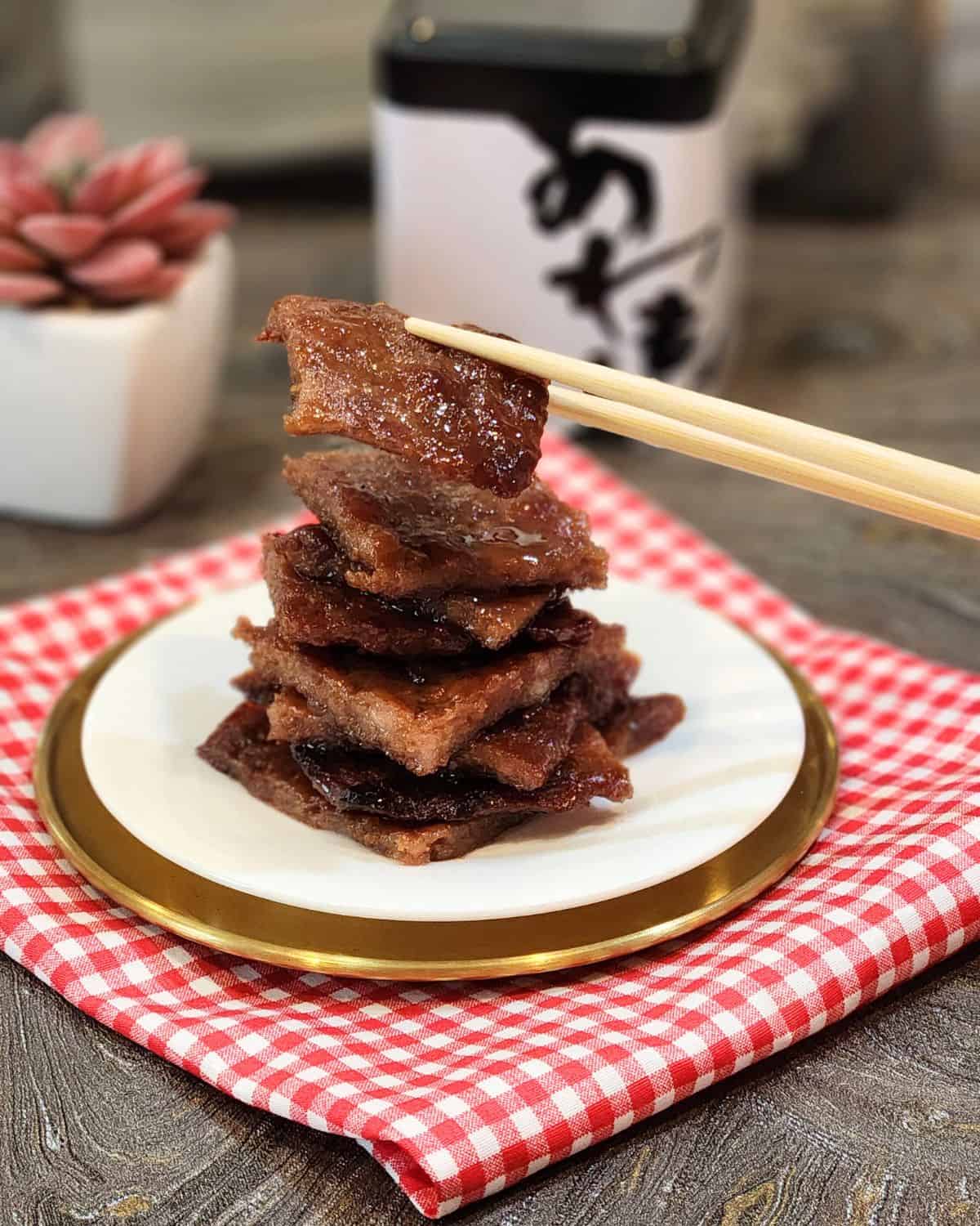 A pair of chopsticks holding a slice of pork jerky.