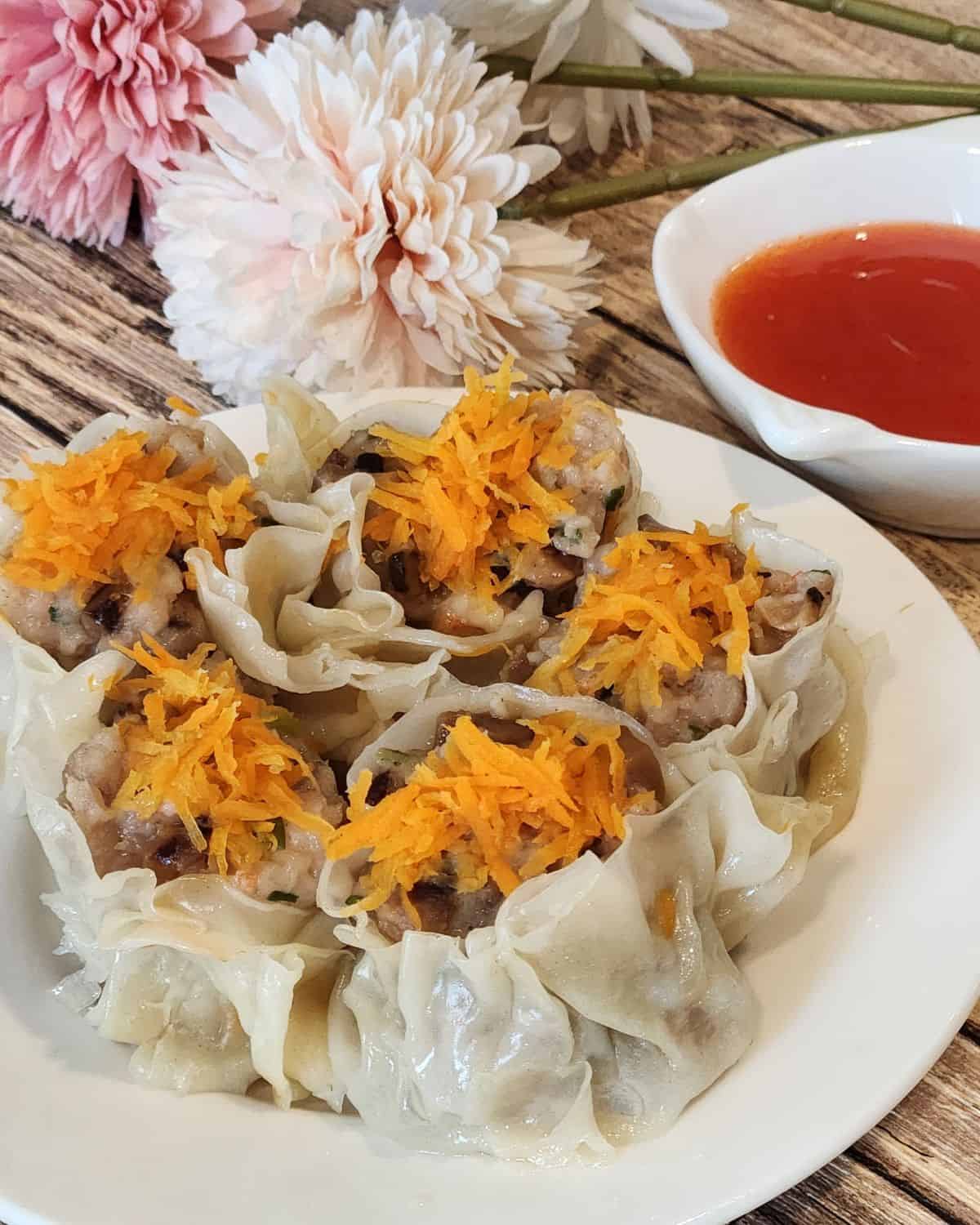 A plate of shao mai with dipping sauce next to it.