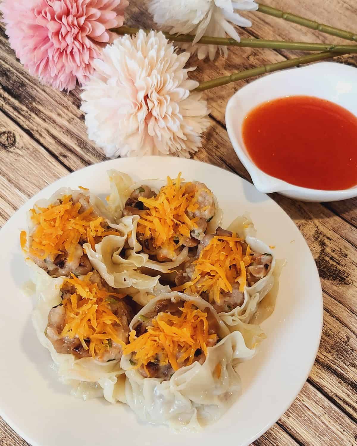 A plate of shu mai with dipping sauce next to it.