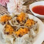 A plate of shao mai with dipping sauce next to it.