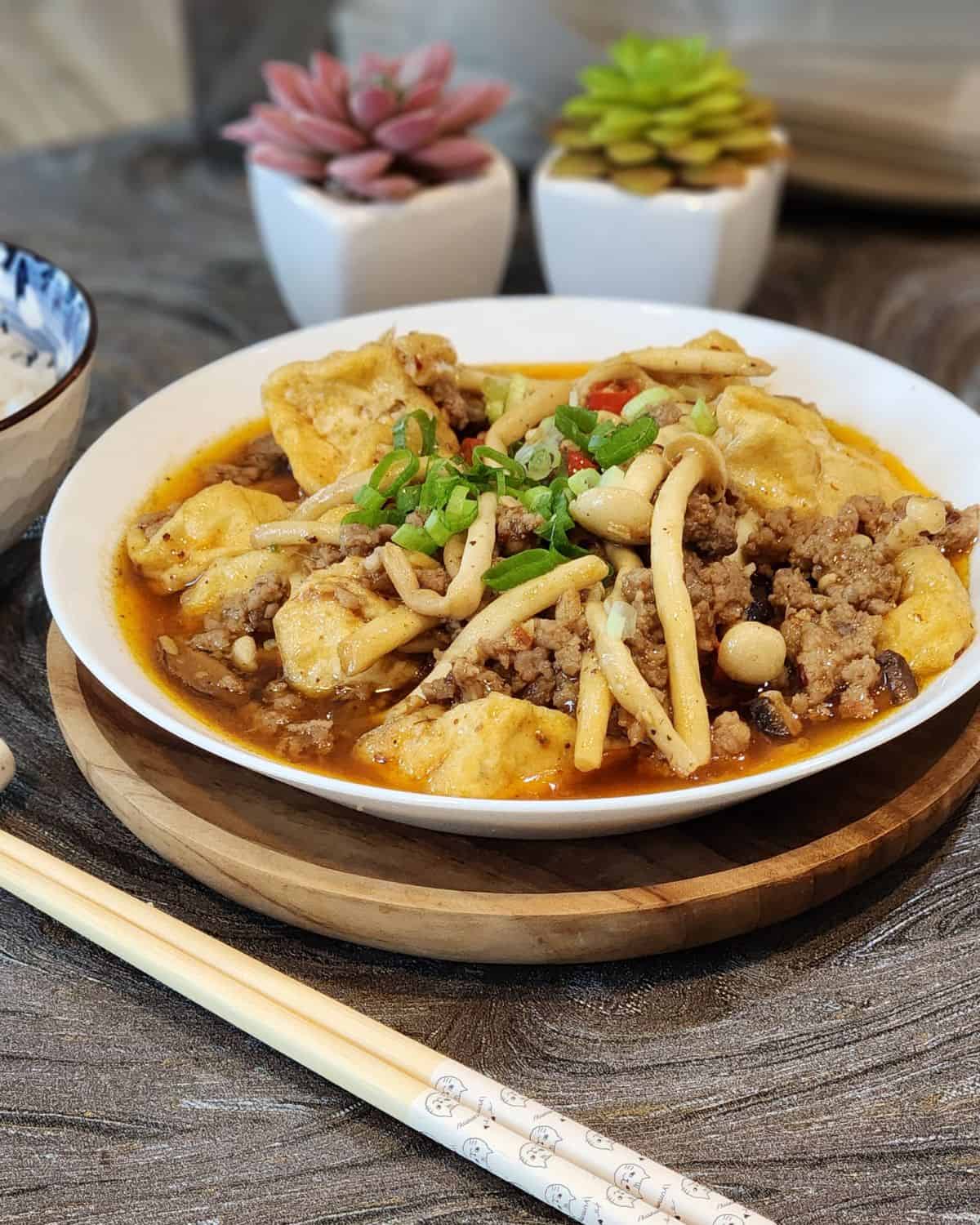 A plate of Szechuan tofu with mushrooms and ground pork with chopsticks.