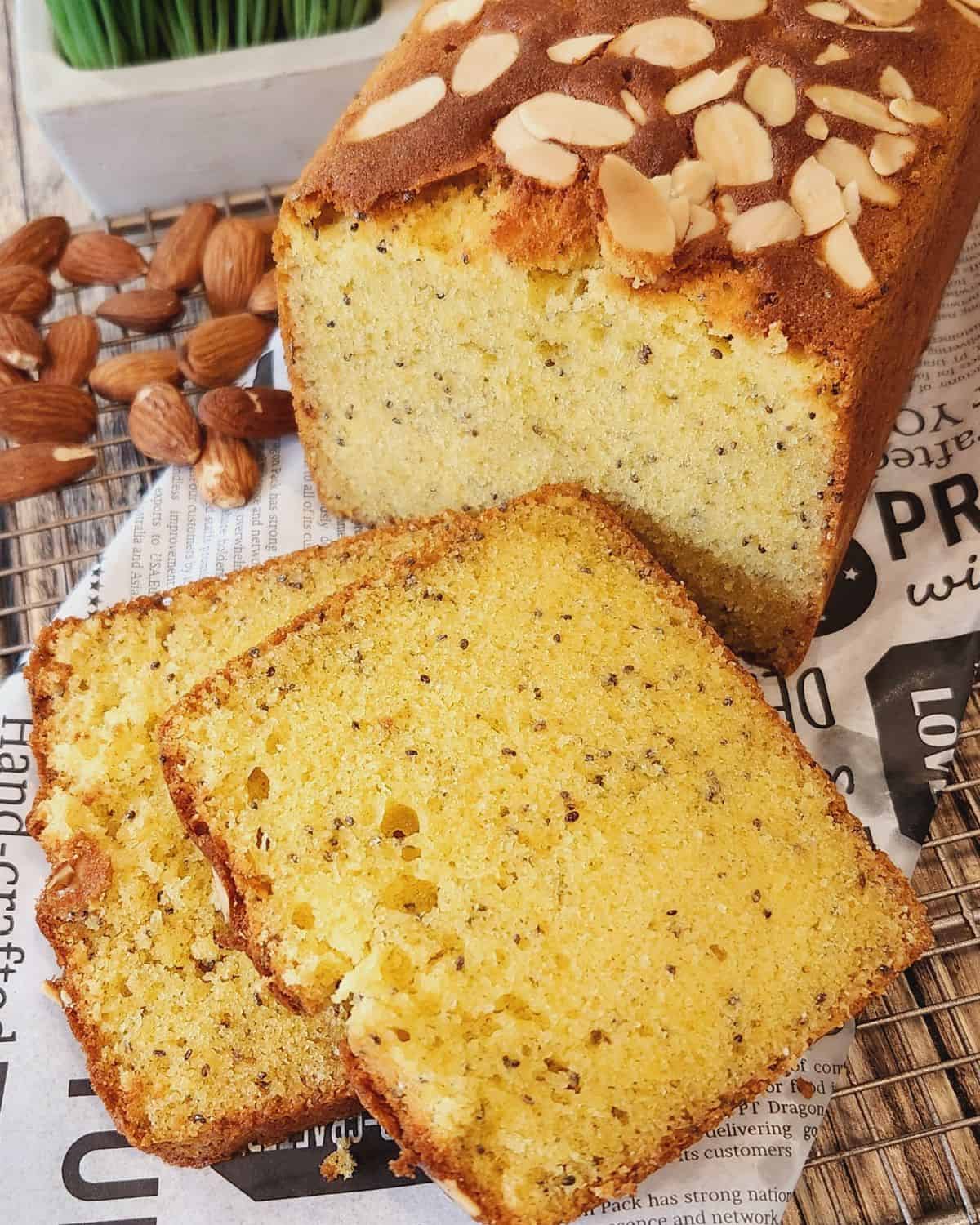 A loaf of Almond Butter Cake with some cake slices on parchment paper.