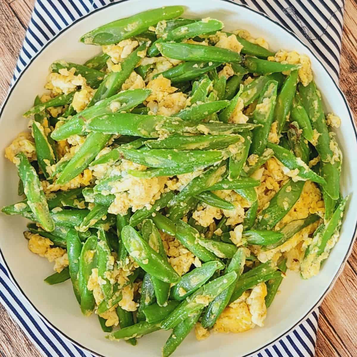 A plate of Asian green beans with garlic on blue-striped napkin.