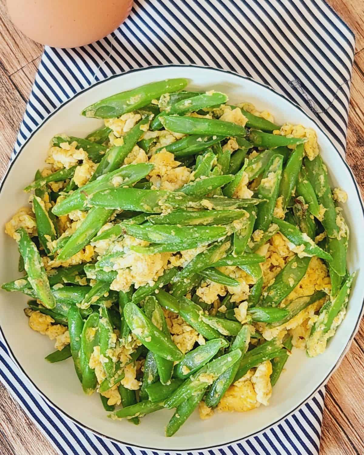 A plate of Asian green beans with garlic on blue-striped napkin.