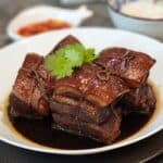 Four cubes of Dong Po Rou in a white bowl with coriander leaves on top.