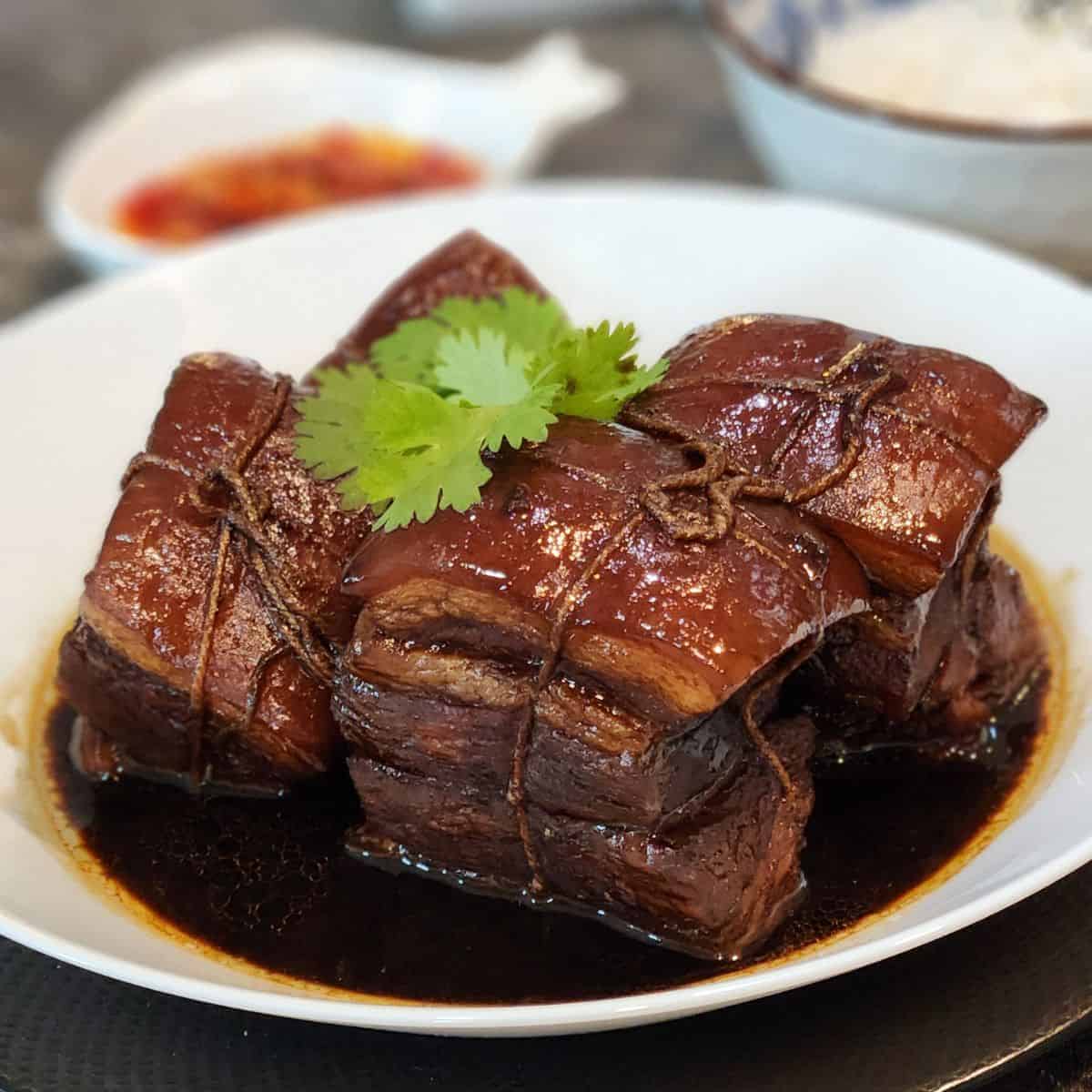Four cubes of Dong Po Rou in a white bowl with coriander leaves on top.
