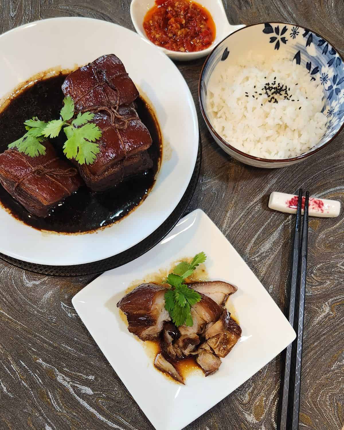 A bowl of rice with chopsticks and a small plate of dong po rou slices.