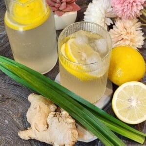A glass of lemon ginger drink with lemon slices and ice.