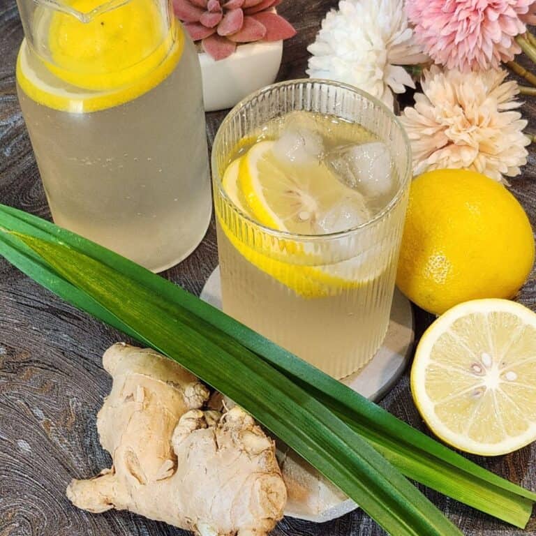 A glass of lemon ginger drink with lemon slices and ice.