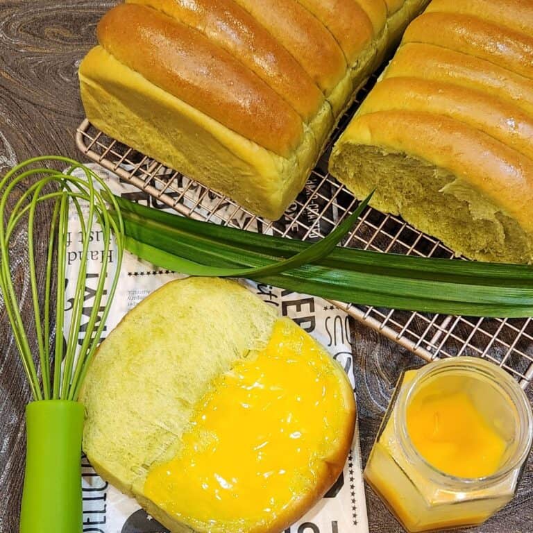 Two loaves of roti sisir pandan on a wire rack with one slice open with coconut jam on it.