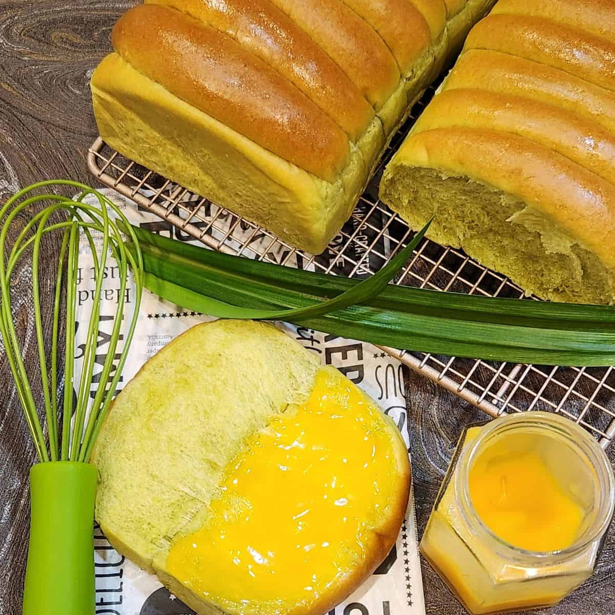 Two loaves of roti sisir pandan on a wire rack with one slice open with coconut jam on it.