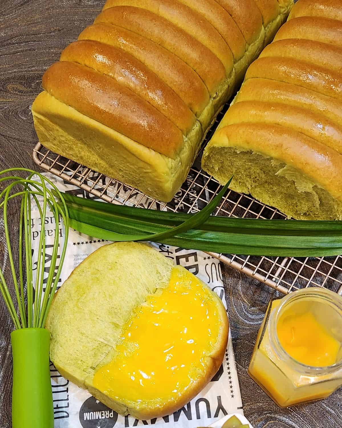 Two loaves of roti sisir pandan on a wire rack with one slice open with coconut jam on it.
