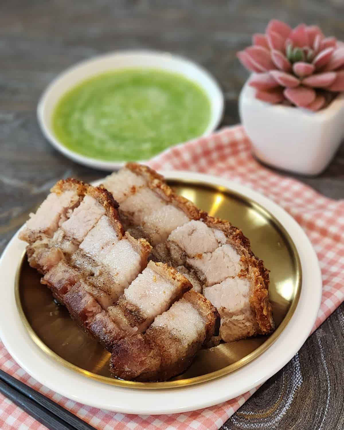 A small plate of neatly lined crispy pork belly with green chilis dipping sauce.