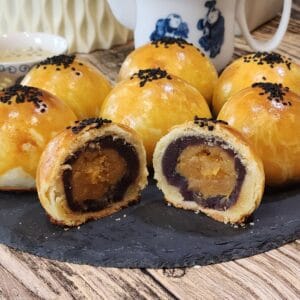 Six salted egg yolk pastry with red bean filling and one sliced open on a black tray.