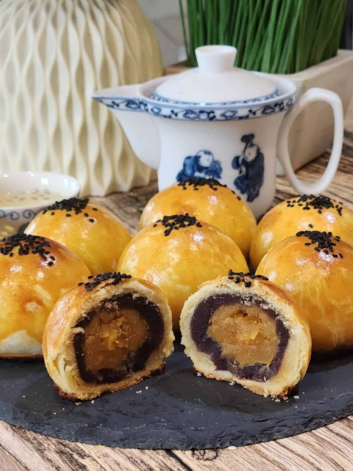 Six salted egg yolk pastry with red bean filling and one sliced open on a black tray.
