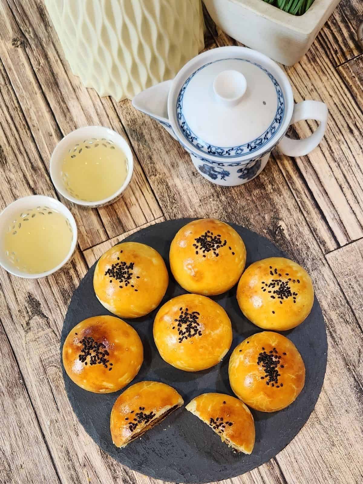 Six salted egg yolk pastry with red bean filling and one sliced open on a black tray.