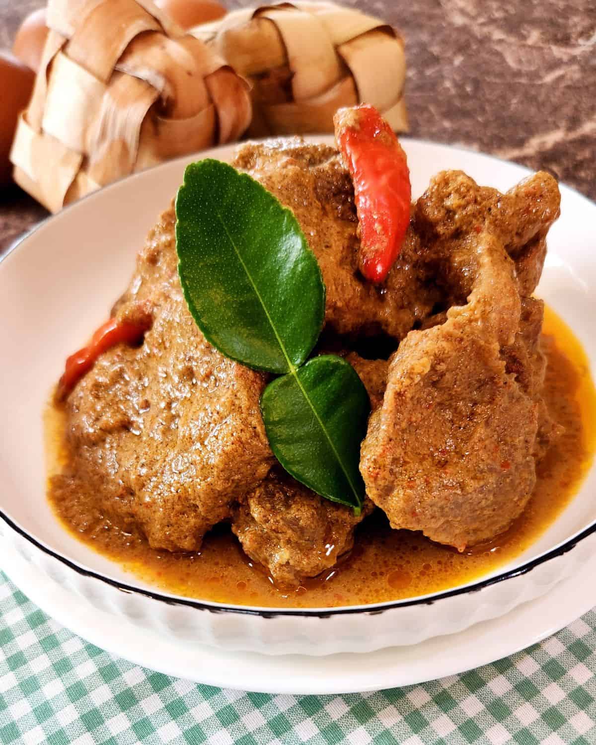 Beef Rendang slices on a plate with lime leaf and chili.