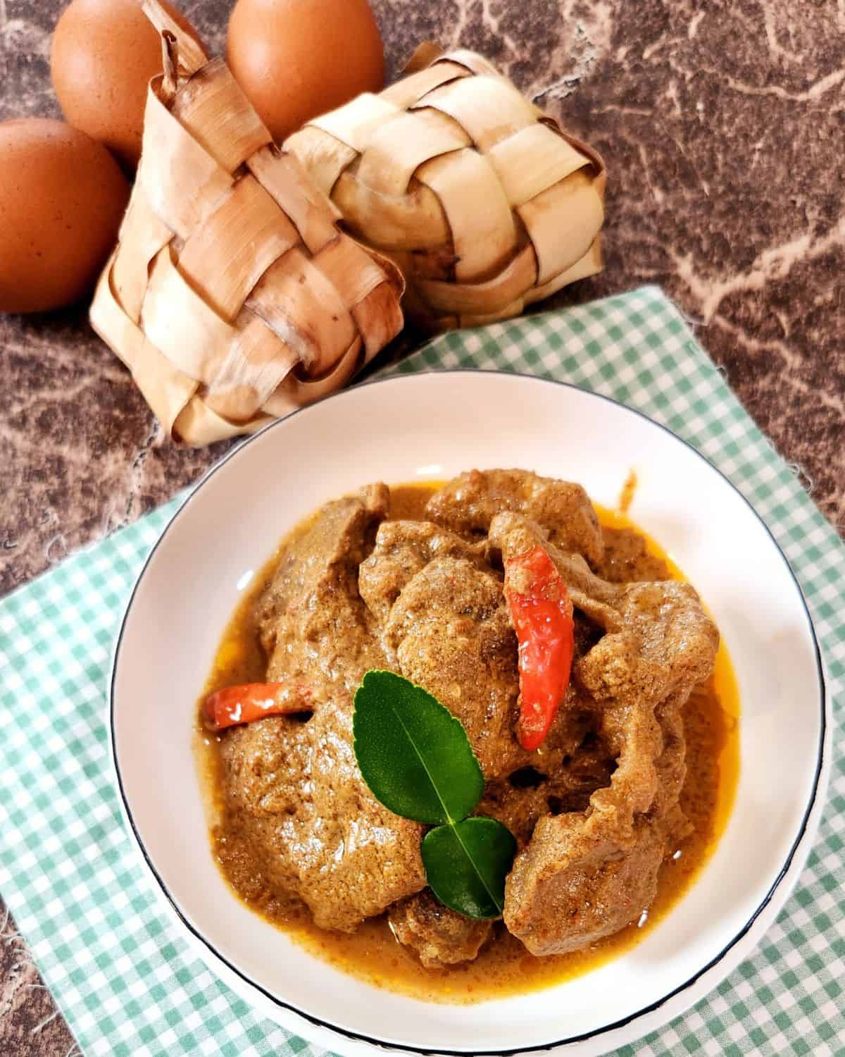 Beef Rendang slices on a plate with lime leaf and chili.