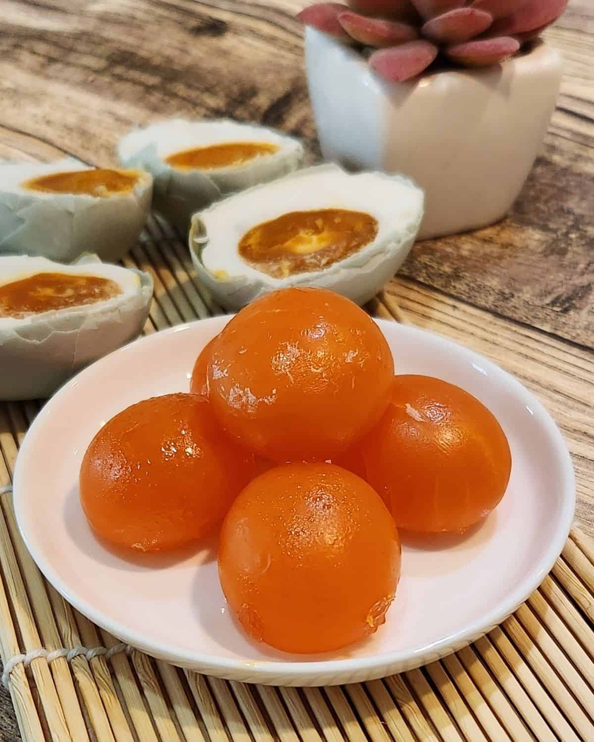 A stack of salted egg yolks on a white plate with cooked salted duck egg yolks at the back.
