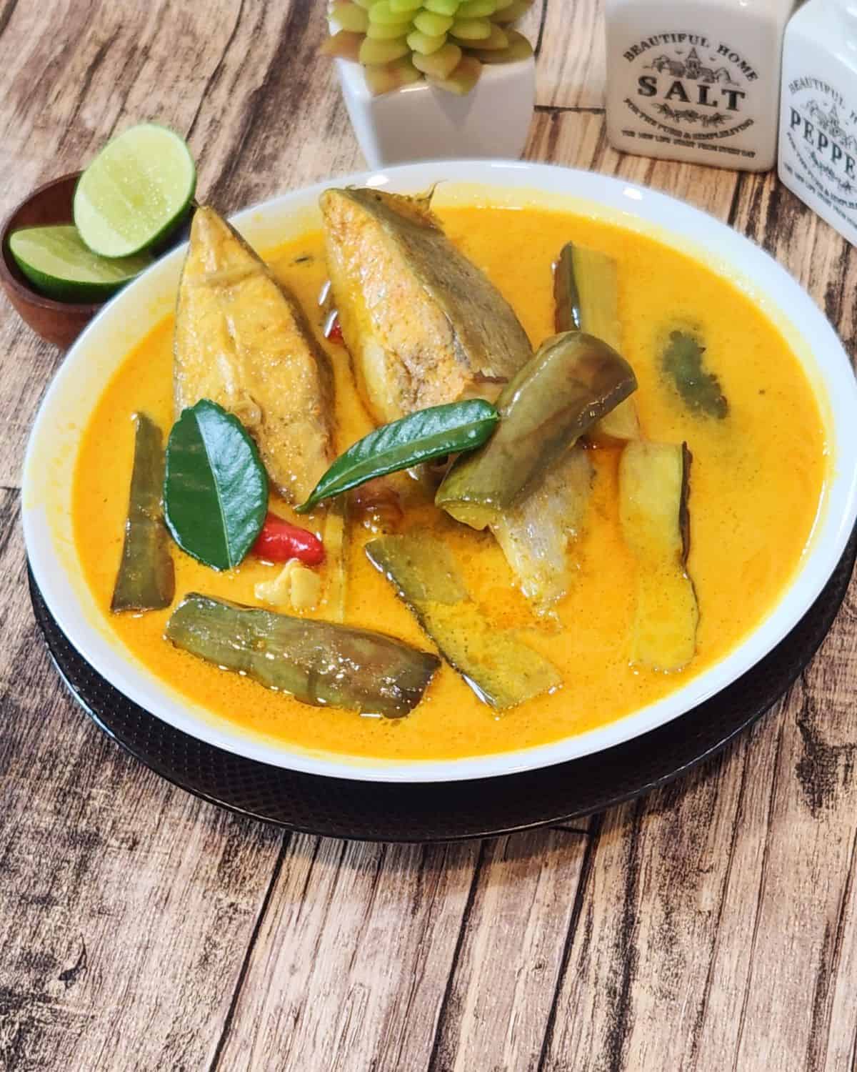 A big bowl of fish curry with lime wedges at the side.