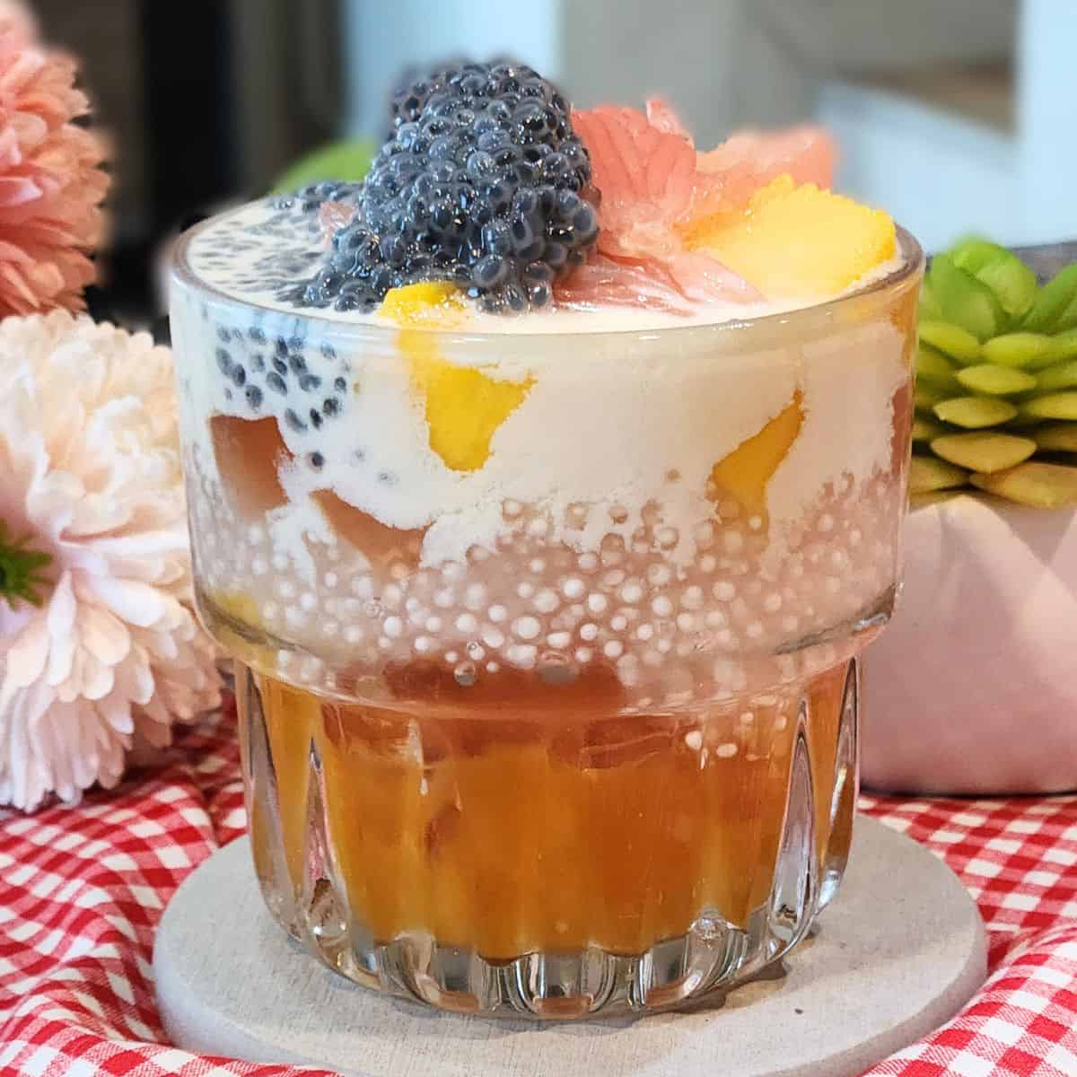 A glass of mango sago dessert with cream cheese mix and pomelo.