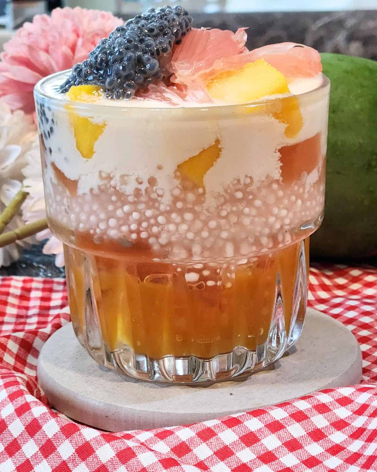 A glass of mango sago dessert with cream cheese mix and pomelo.