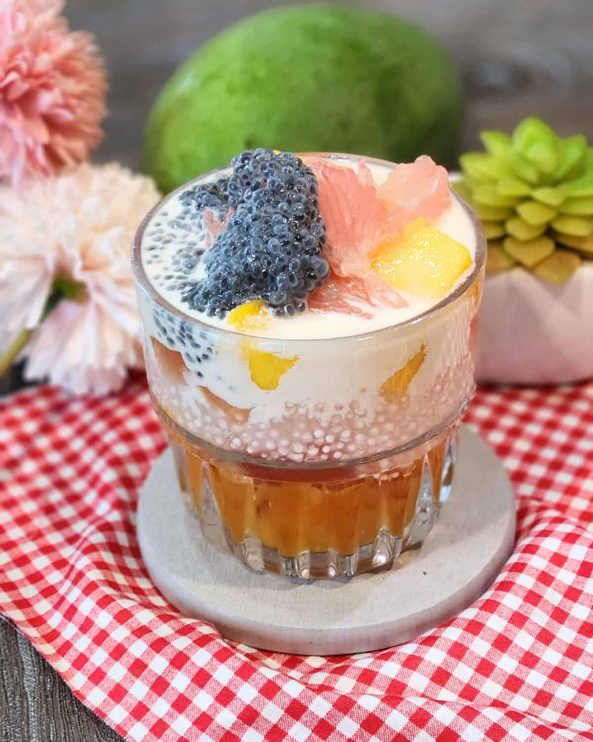 A glass of mango sago dessert with cream cheese mix and pomelo.