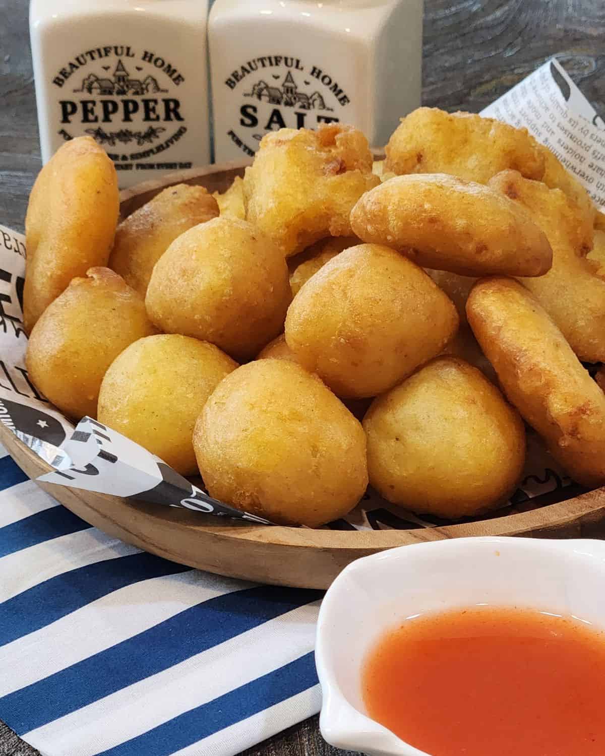 A stack of Fried Mashed Potato Patties on a wooden plate with tomato sauce.