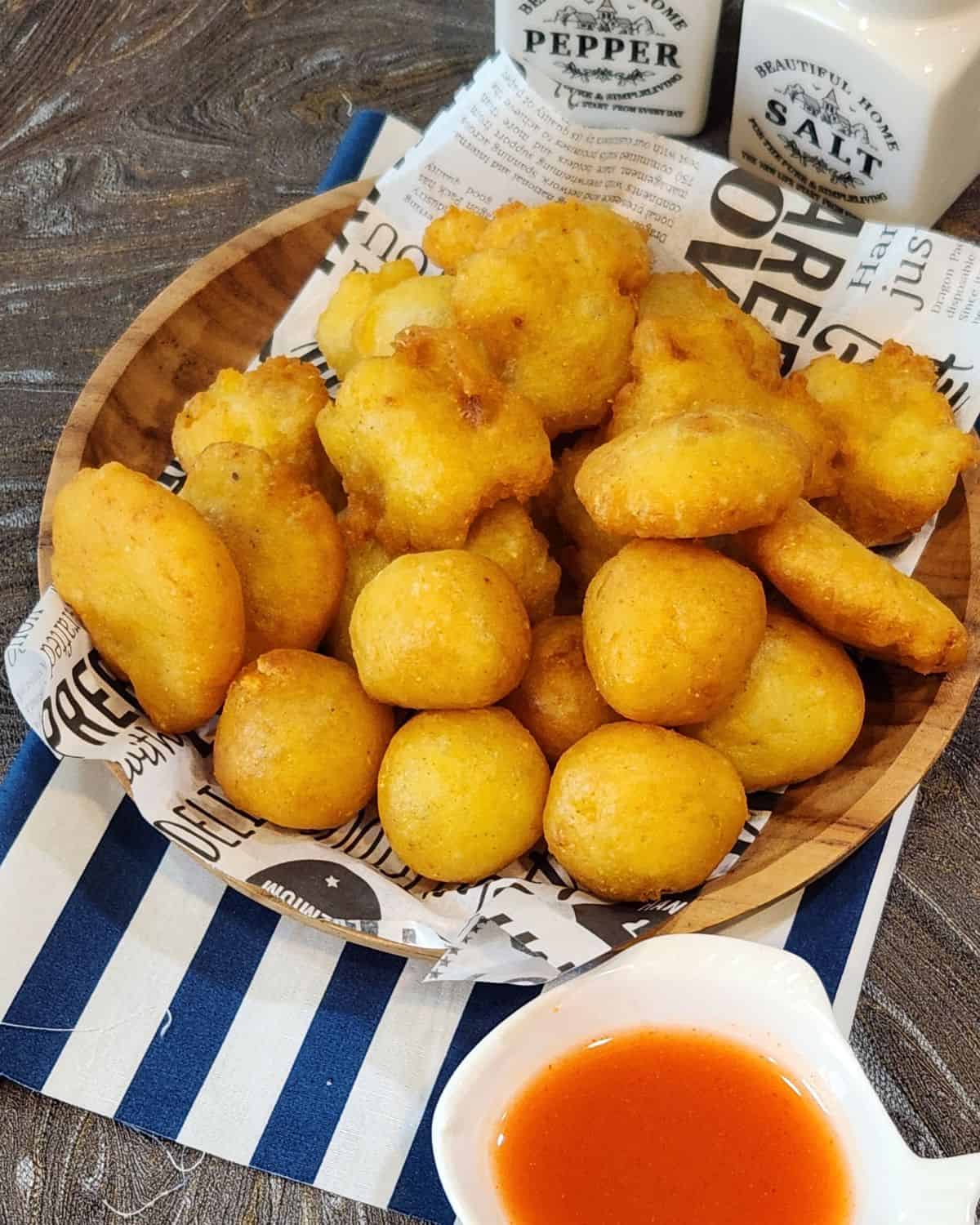 A stack of Fried Mashed Potato Patties on a wooden plate with tomato sauce.
