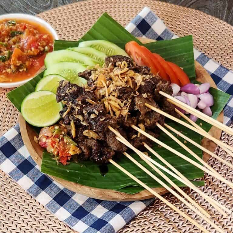 A stack of sate maranggi, Indonesian beef satay on banana leaves with the chili sauce and condiments.