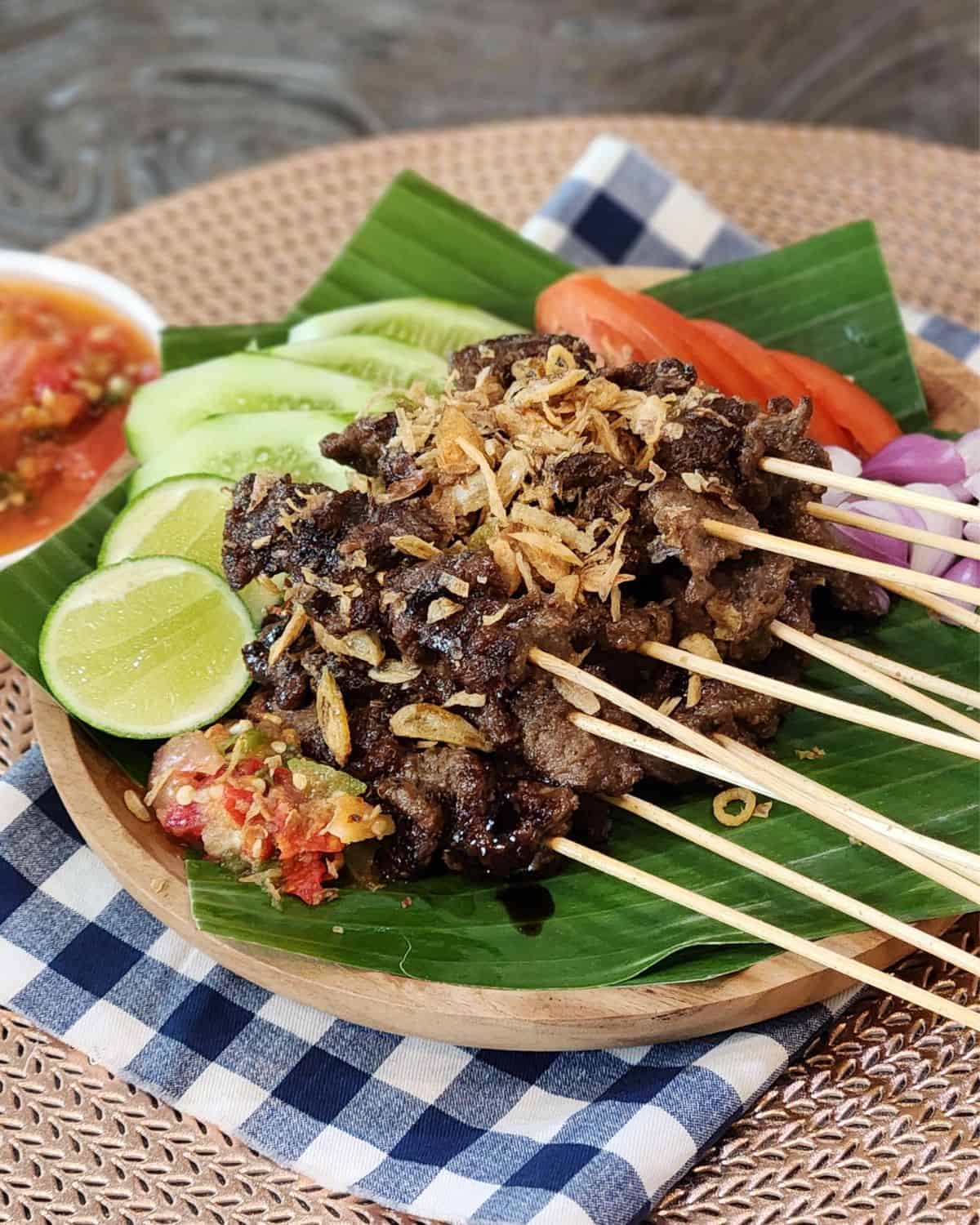 A stack of sate maranggi, Indonesian beef satay on banana leaves with the chili sauce and condiments.