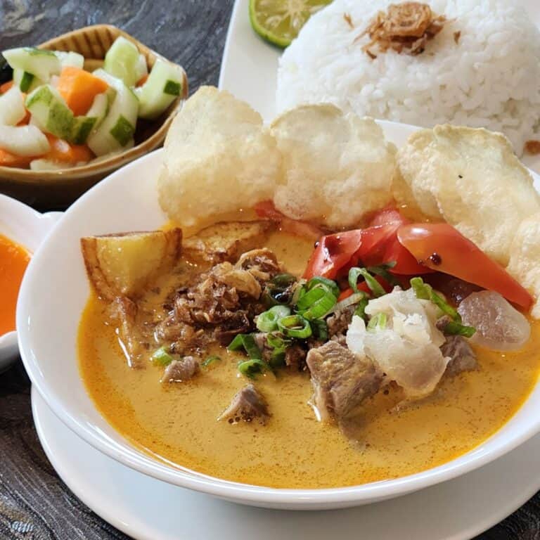 A bowl of soto tangkar, Indonesian beef coconut soup with crackers, steamed white rice, sambal, and pickles.