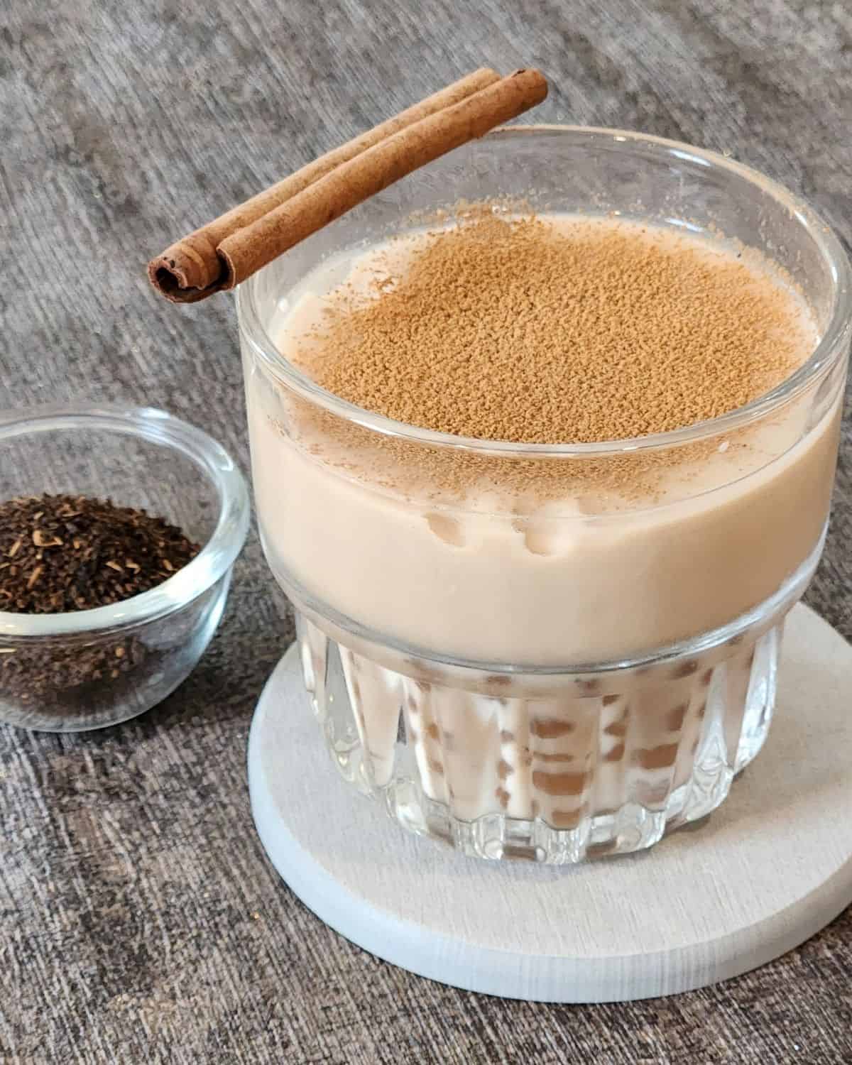 A glass of Assam milk tea with dusts of cinnamon powder and a cinnamon stick for garnish.