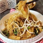 A pair of chopsticks holding bihun goreng from a plate.