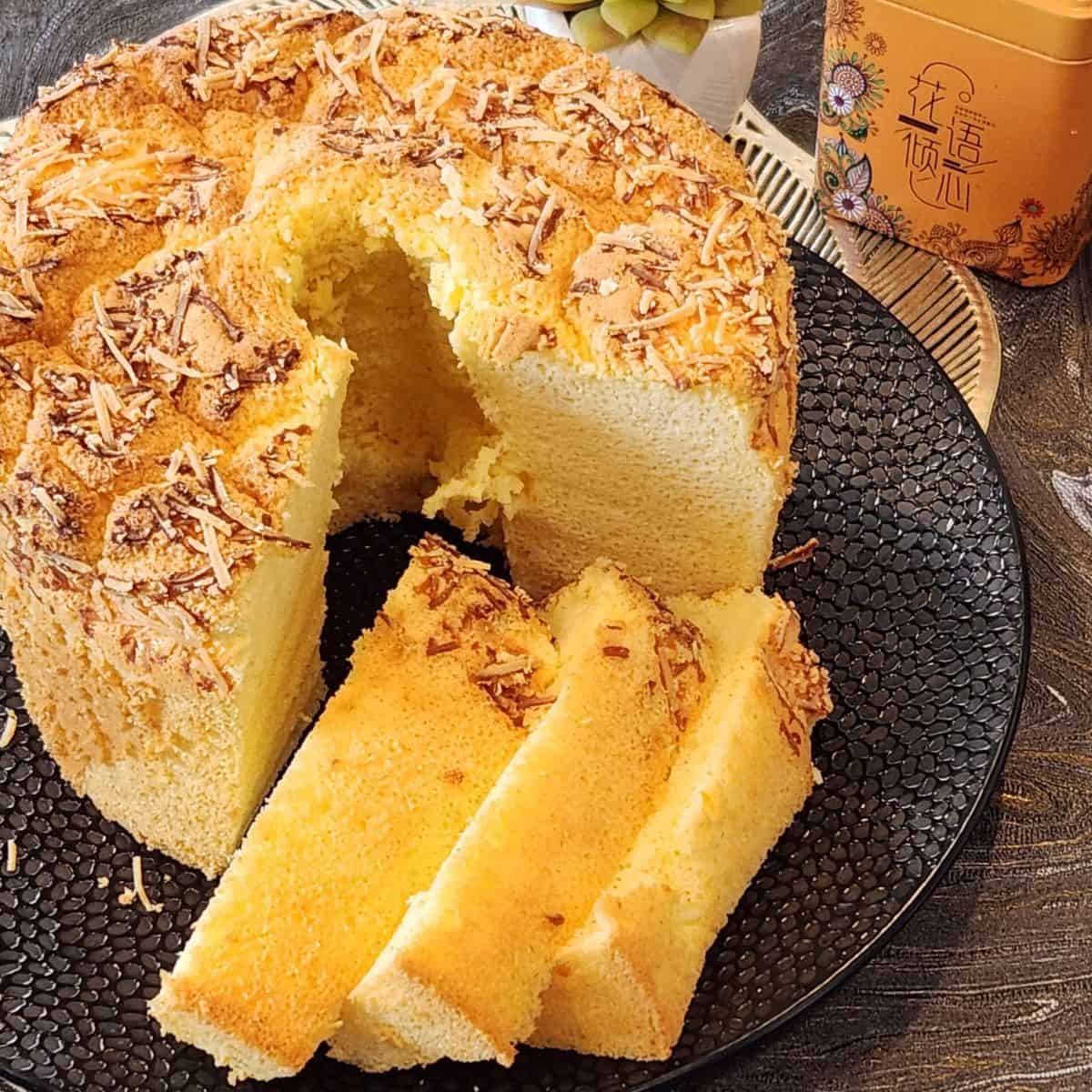 Cheese chiffon cake with a few slices on a black plate.