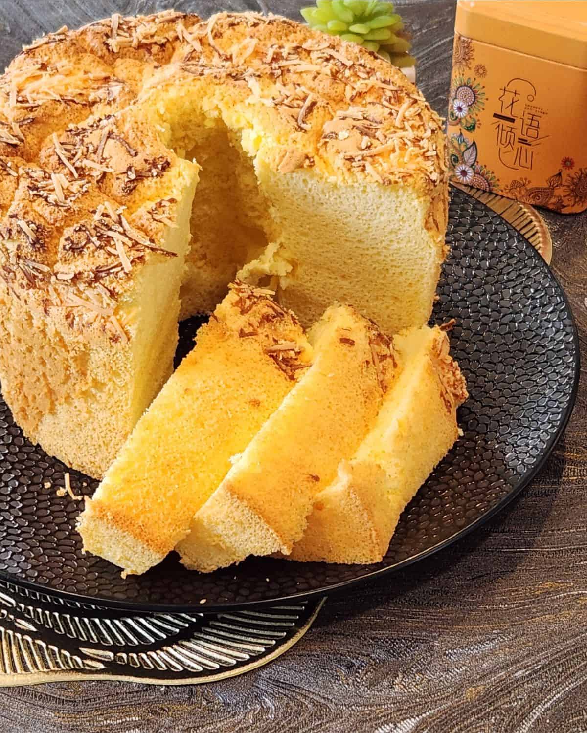 Cheese chiffon cake with a few slices on a black plate.