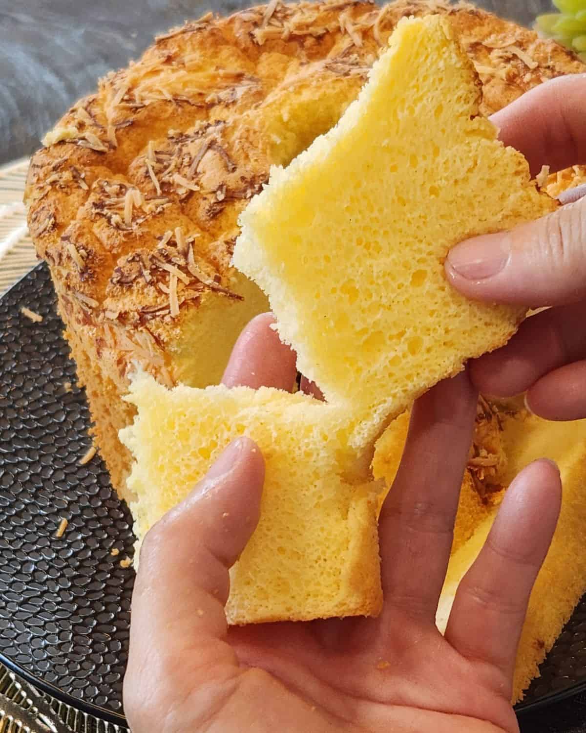 A slice cheese chiffon cake torn into two revealing the fluffy texture.