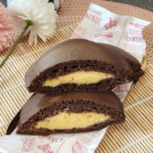A stack of Chocolate dorayaki with custard filling on parchment paper.