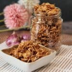 A small plate full of crispy fried shallots with a jar full of bawang goreng at the back.