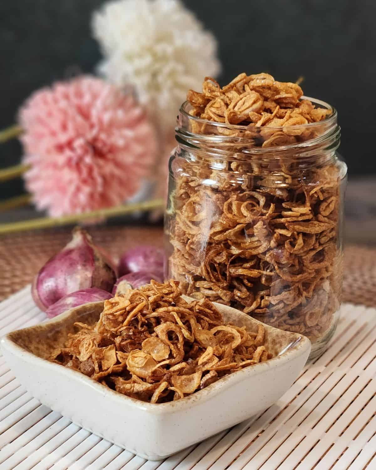 A jar of crispy fried shallots and a small plate full of bawang goreng.