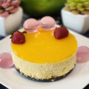 No Bake mango cheesecake decorated with jelly and strawberries on a plate.