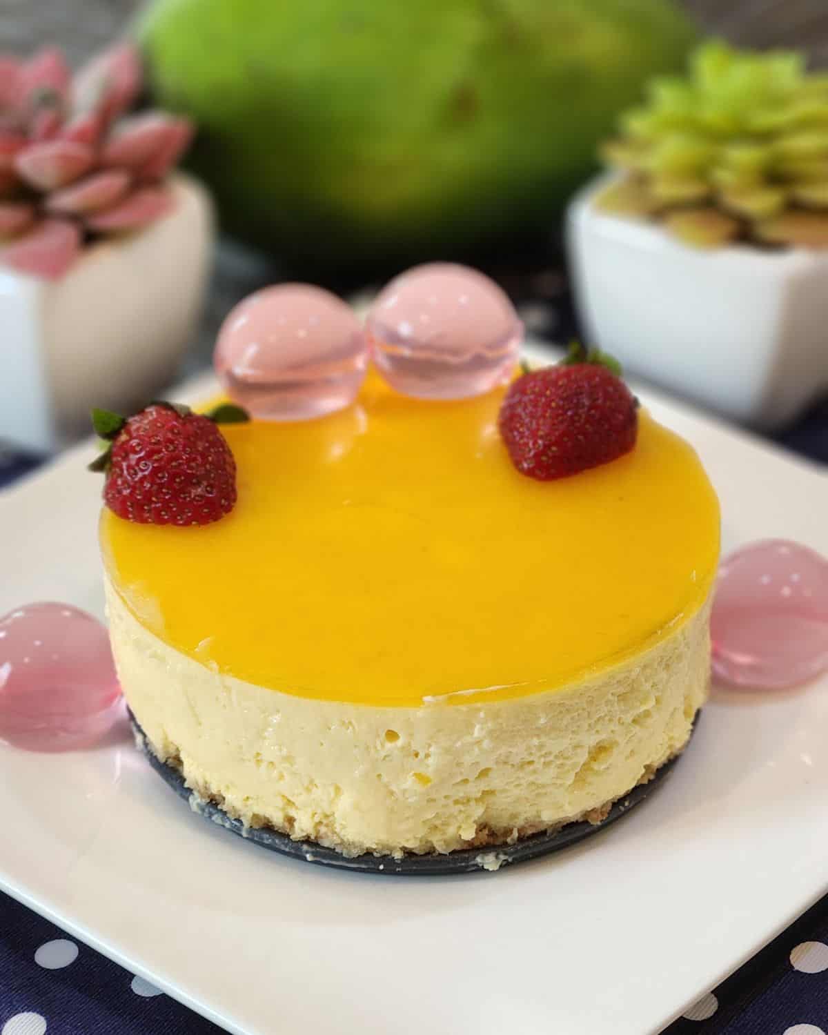 A plate with no bake mango cheesecake, decorated with strawberries and jelly.