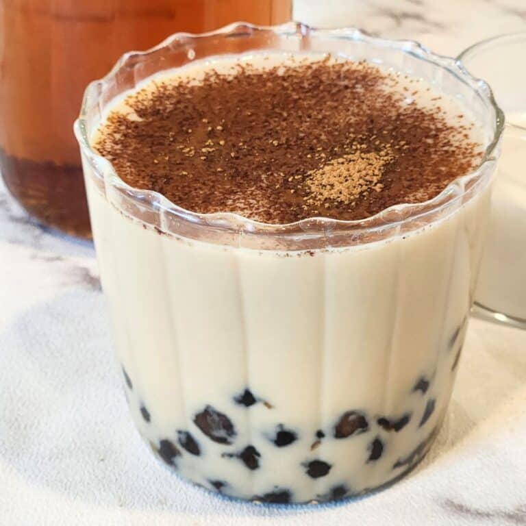 A glass of oolong milk tea with tapioca pearls and ground cinnamon.