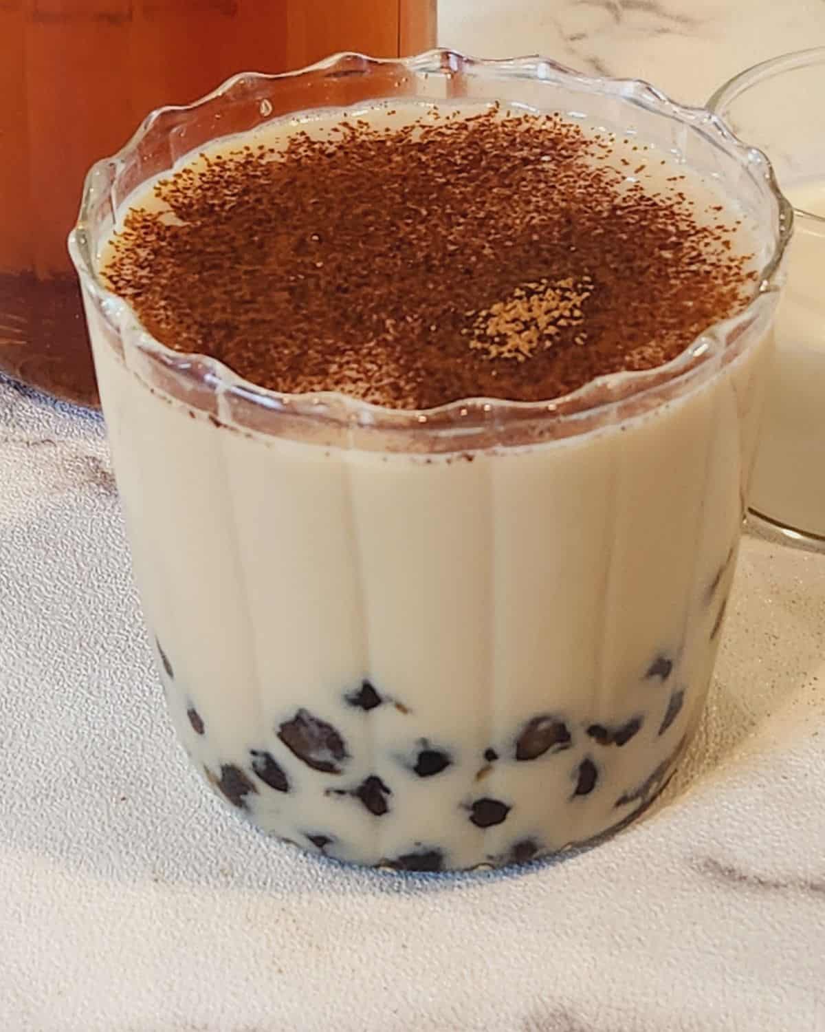 A glass of oolong milk tea with tapioca pearls and ground cinnamon.